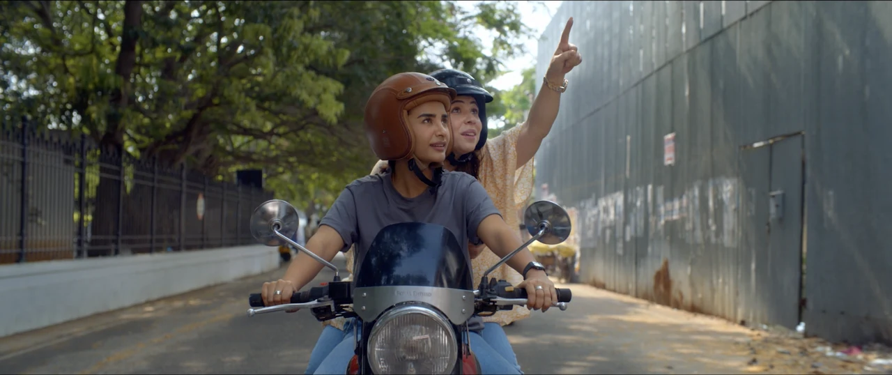 Two helmeted riders on a scooter in a film scene.