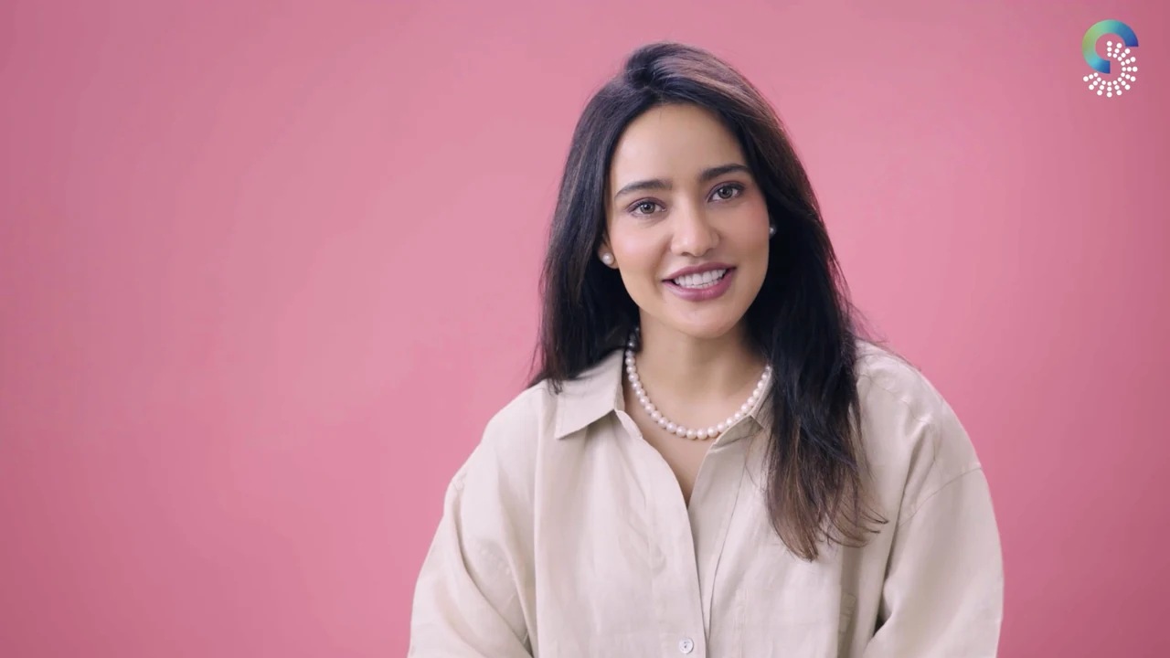 A woman speaking to camera against a pink studio background.